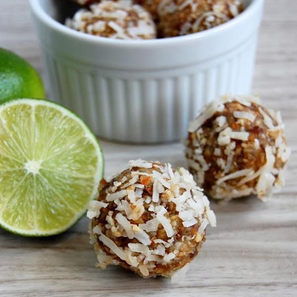 Coconut-covered energy bites with a sliced lime and a white bowl in the background.