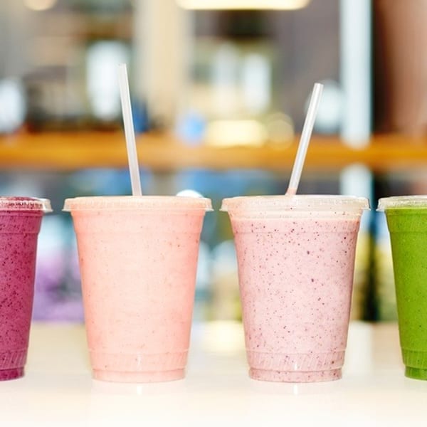 Four colorful smoothies in clear plastic cups with straws, including purple, pink, and green.
