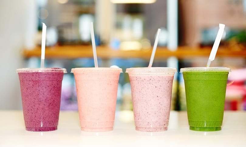 Four colorful smoothies in clear plastic cups with straws, including purple, pink, and green.