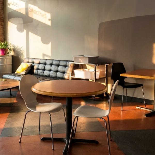 Sunlit cafe interior with black couches, round tables, and colorful floor tiles.
