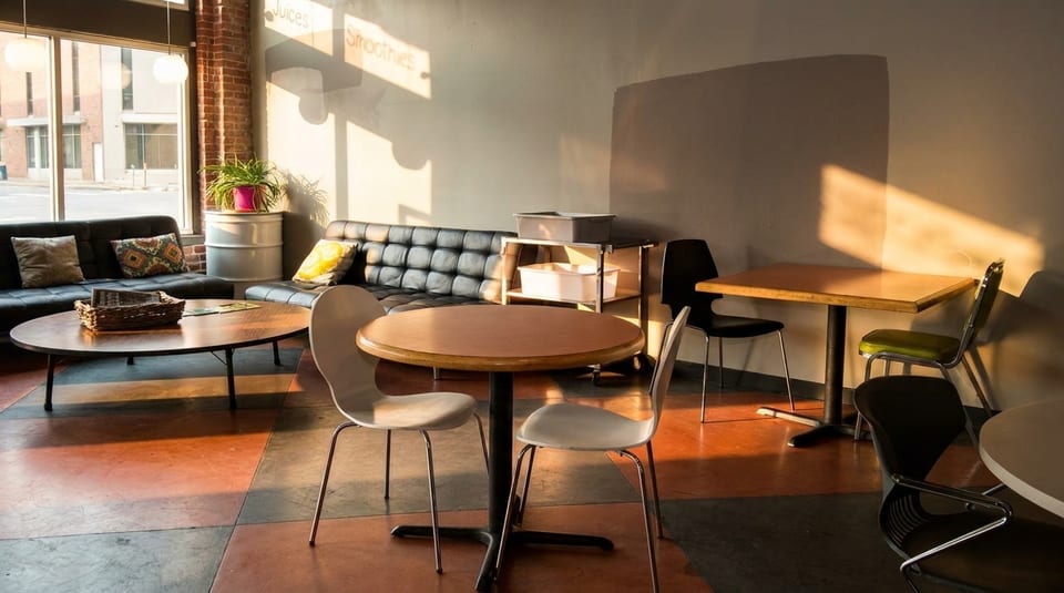 Sunlit cafe interior with black couches, round tables, and colorful floor tiles.