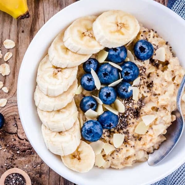 Oatmeal topped with sliced bananas, blueberries, chia seeds, and almond flakes in a white bowl.
