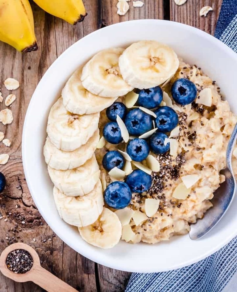 Oatmeal topped with sliced bananas, blueberries, chia seeds, and almond flakes in a white bowl.