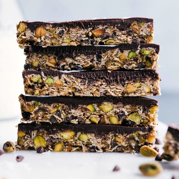Stack of five chocolate-topped granola bars with pistachios and almonds on a white surface.