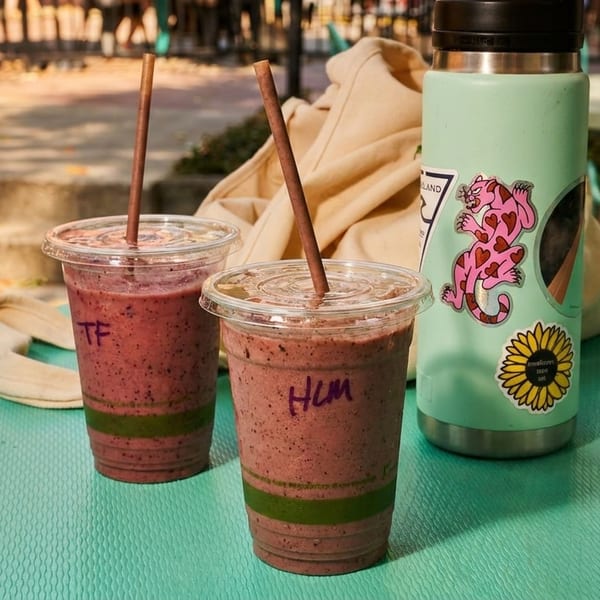 Two berry smoothies with straws and a mint green water bottle on an outdoor table.