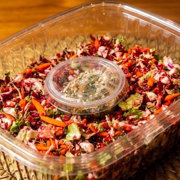 Colorful chopped salad with dressing in a clear plastic container on a gold placemat.